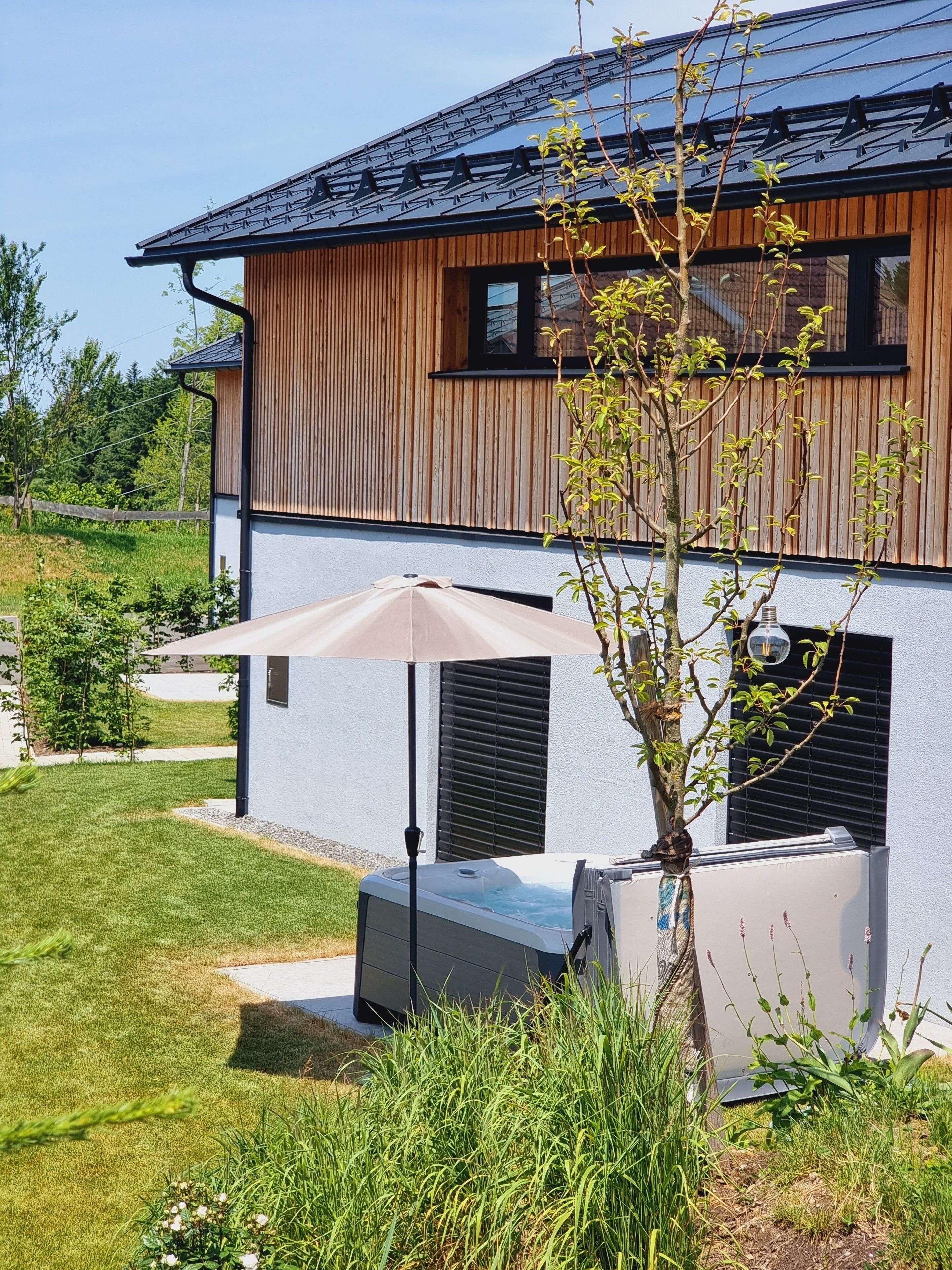 A modern house with a wooden exterior, a hot tub, and a patio umbrella.