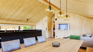 A modern kitchen with wooden cabinets, a dining area with a wooden table and chairs, and a living area with a sofa and a television. - Pfänder Glück (Lochau)