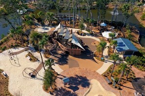 Luchtbeeld van een park met een zandgebied, een waterpartij en een beschaduwd paviljoen.