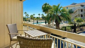 A balcony with wicker furniture, a pool, and palm trees. - Luxury Oceanfront Villa, w/ Pool on Hilton Head (Hilton Head Island)