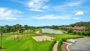 A golf course with a pond, palm trees, and a parking area with a building in the background. - On the Sea Palms Golf Course. 18th Hole, Fairway and Lagoon frontage (Saint Simons Island)