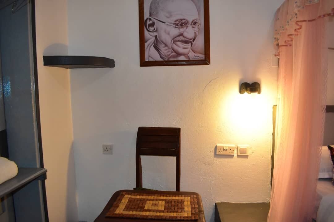 A room with a bed, a chair, a bedside table, a wall-mounted light, and a framed picture.