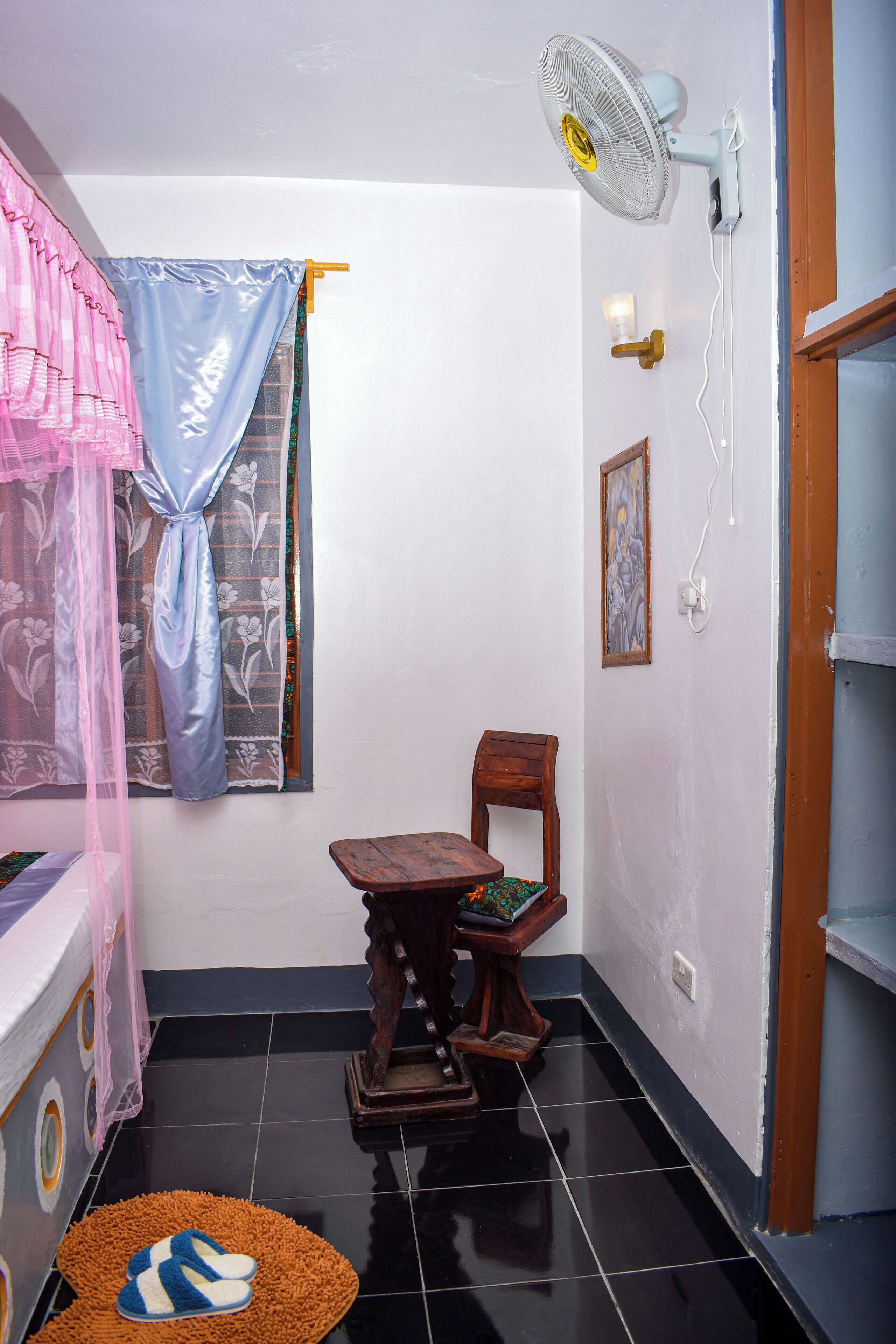 Una habitación pequeña con una cama, un ventilador, una silla y una mesita.