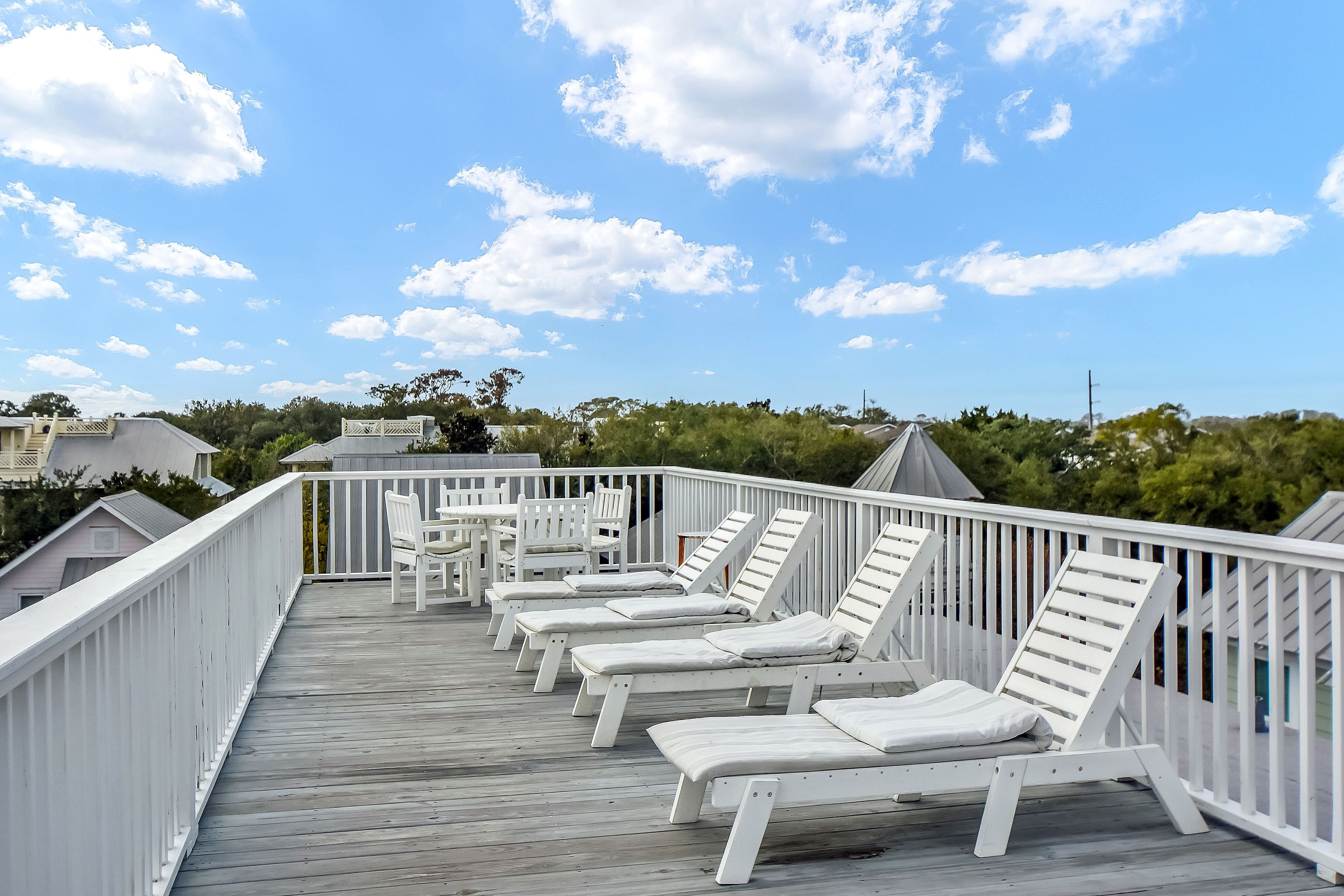 A wooden deck with white railings and multiple sun loungers.