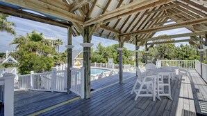 Eine überdachte Holzterrasse mit weißen Geländern, einem Pool und Gartenmöbeln.