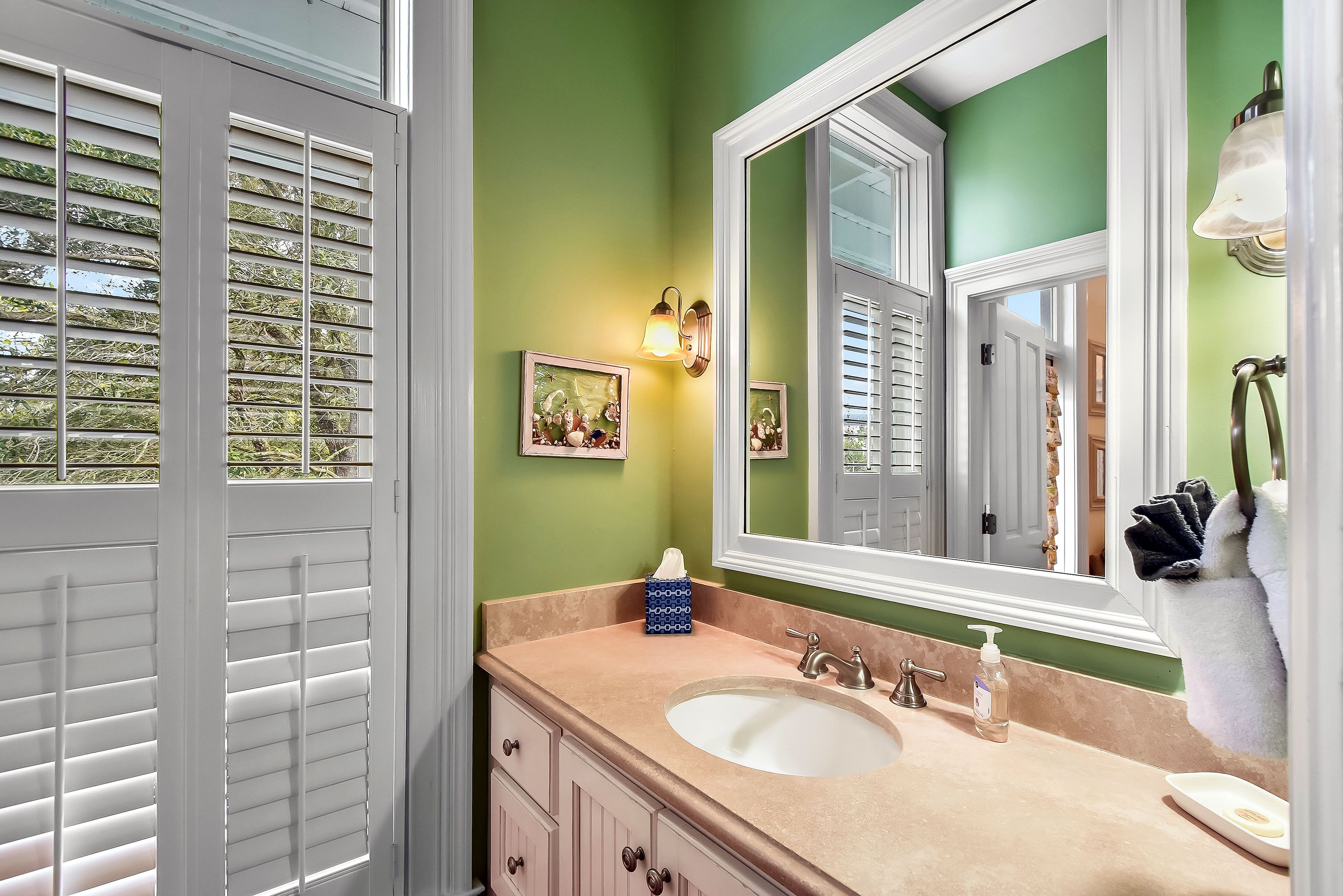A bathroom with a beige sink, green walls, and a large mirror.