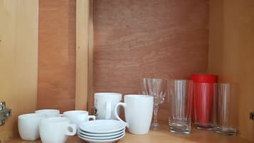 A wooden cabinet with white and clear glassware, including mugs, plates, and glasses.