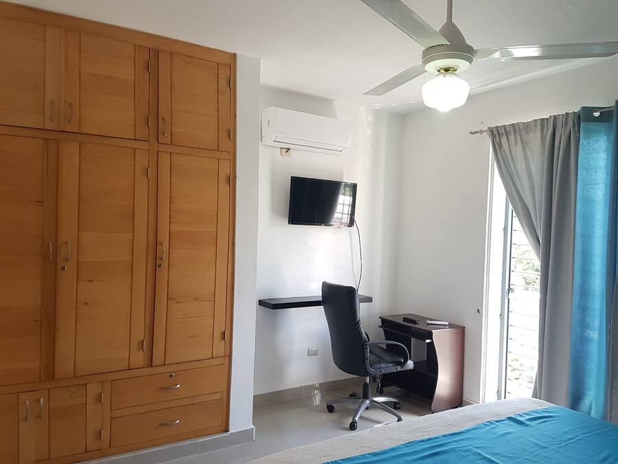 Un dormitorio con cama, escritorio, silla, armario, ventilador de techo y televisión.