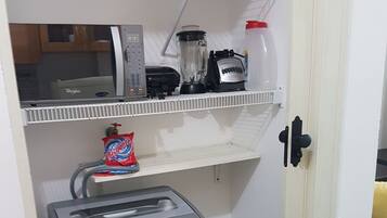 Una piccola cucina accessoriata con frigorifero, macchina del caffè, frullatore e un ripiano con una busta di patatine.