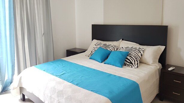 A bedroom with a bed, nightstands, a ceiling fan, and a window with curtains. - Bello y céntrico (Santiago de los Caballeros)