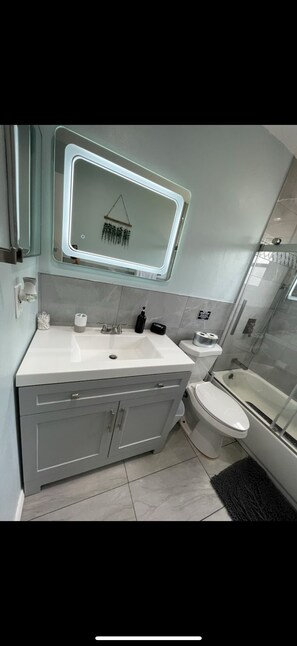 A modern bathroom with a large mirror, a toilet, a sink, and a bathtub. - Cozy chic pool house 4 bed 2 bath KING BED in master bedroom (Bradenton)