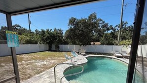 A covered outdoor swimming pool with a tiled deck, a pool ladder, and lounge chairs. - Cozy chic pool house 4 bed 2 bath KING BED in master bedroom (Bradenton)