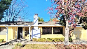 Una casa de dos pisos con garaje, chimenea y un árbol con hojas otoñales.