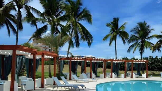Ein Poolbereich mit Liegestühlen und einer Pergola mit Vorhängen, umgeben von Palmen.