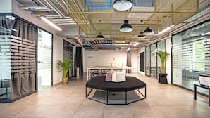 A modern office space with a central black table, glass walls, and potted plants.