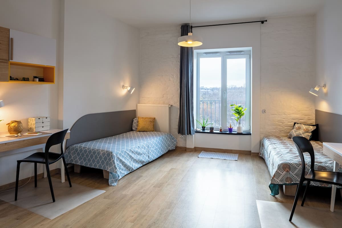 Habitación pequeña con una cama individual, un escritorio y una silla. Hay una ventana con vista al exterior.