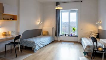 A compact bedroom with a single bed, a desk, and a chair. There is a window with a view of the outside.