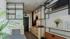 A modern bedroom with a bed, a desk, and a kitchenette.