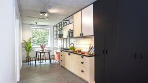 A modern kitchen with a dining area, featuring a large window, a potted plant, and a tiled floor.