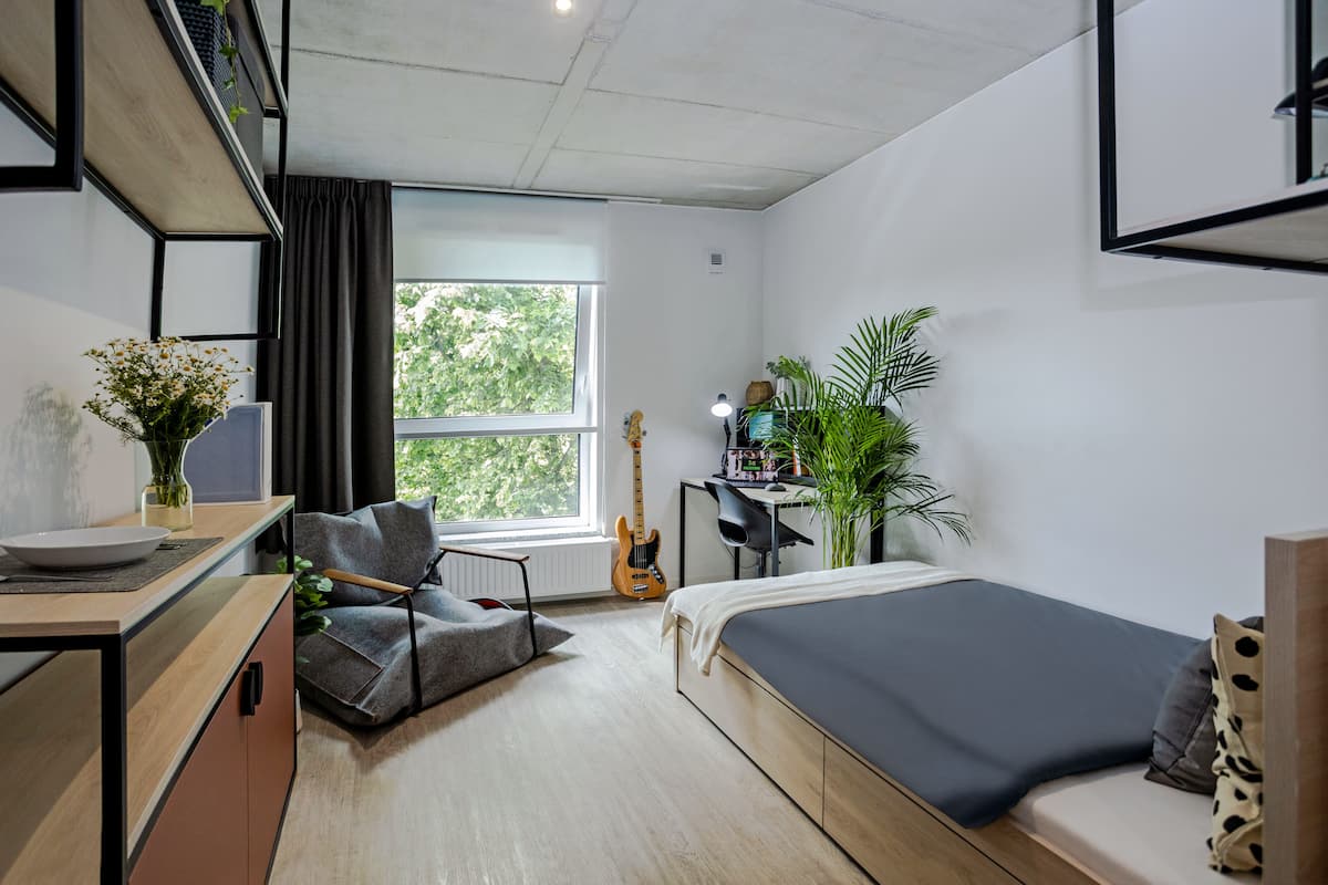 Un dormitorio moderno con una cama, un escritorio, una silla, una guitarra y un ventanal grande.