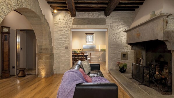 A cozy living room with a fireplace, stone walls, and a dining area visible through an archway. - Villa La Rassinata 12, Emma Villas (Arezzo)