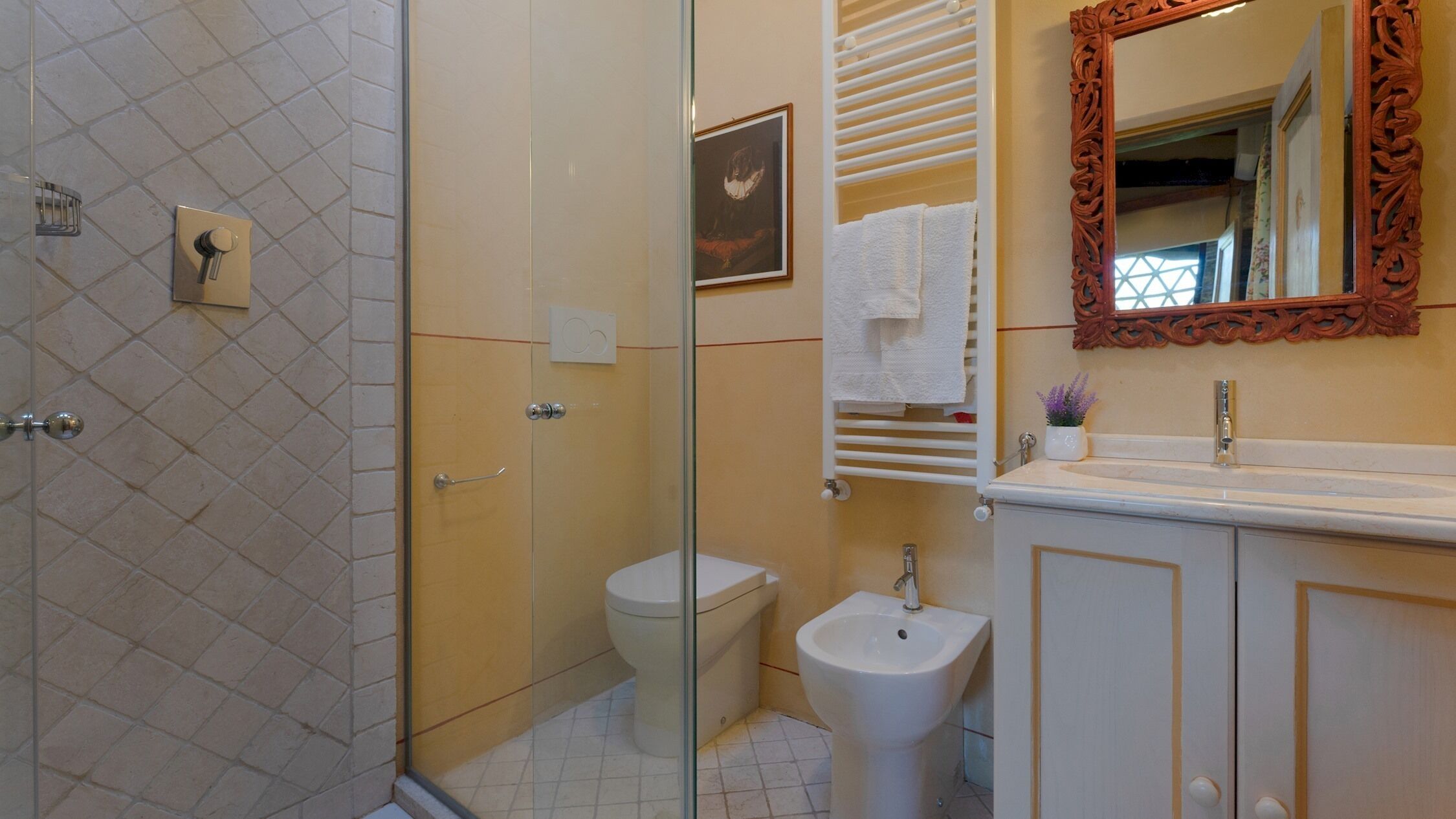 A bathroom with a glass shower enclosure, a toilet, a bidet, a sink, and a mirror with an ornate frame.