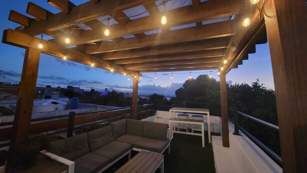 An outdoor patio with wooden pergola, string lights, a sofa, and a table.