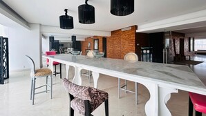 Un comedor moderno con una mesa blanca alargada, sillas estampadas y lámparas colgantes negras.
