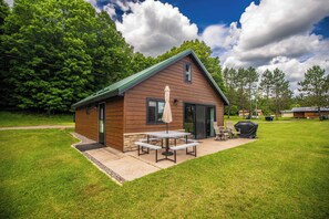 A small wooden cabin with a patio, a covered table and chairs, and a barbecue grill. - Waterfront Butternut Lake Getaway - With Dock! (Butternut)