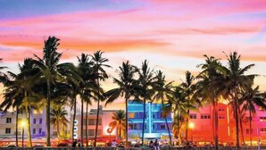 A beachside hotel with palm trees, colorful buildings, and a sunset sky.