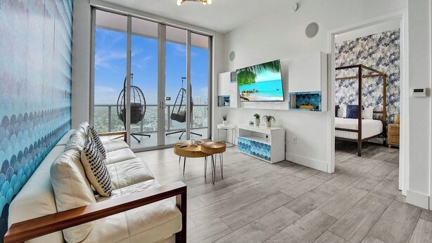 A modern living room with a sofa, a TV, and a balcony with a view of the city.
