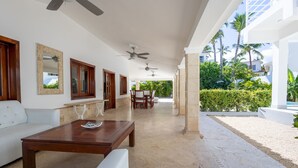 Un espace intérieur spacieux doté d’un ventilateur de plafond, d’une table basse en bois, de canapés blancs et d’un coin repas avec des chaises.