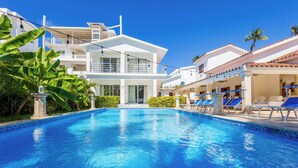 Une piscine à l’eau d’un bleu limpide, entourée de bâtiments blancs dotés de balcons, et agrémentée de quelques palmiers.