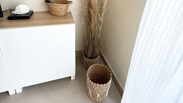 A clean, minimalist room with a wooden bench, a coat rack with hooks, a woven basket, and tall grasses. - Apartment with garden - sea view (Palavas-les-Flots)