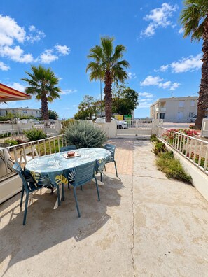 Une terrasse extérieure avec une table ronde et des chaises, des palmiers et une vue sur les bâtiments en arrière-plan.