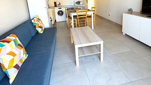 A compact living space with a sofa, a dining table, a kitchen area, and a television. - Apartment with garden - sea view (Palavas-les-Flots)