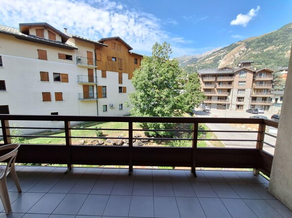 A balcony with a view of multi-story buildings, a tree, and a mountainous landscape.