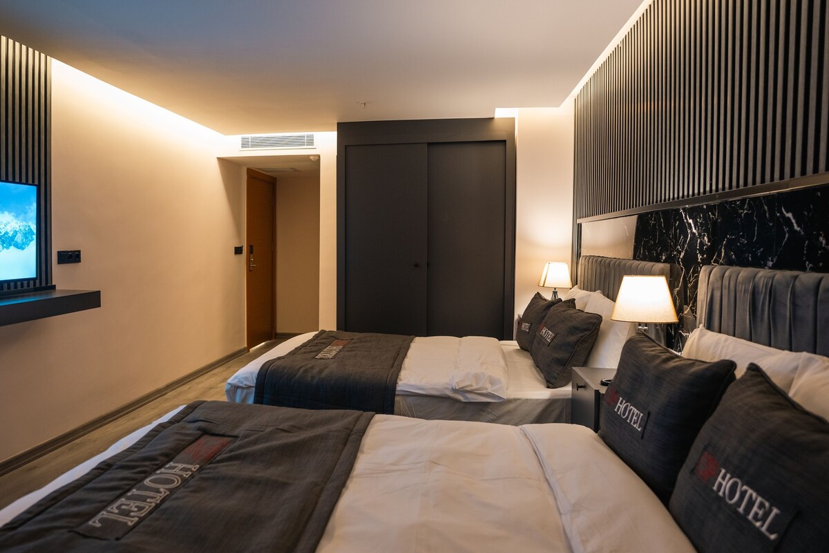 A hotel room with two beds, a TV on the wall, a door, and a nightstand with a lamp.