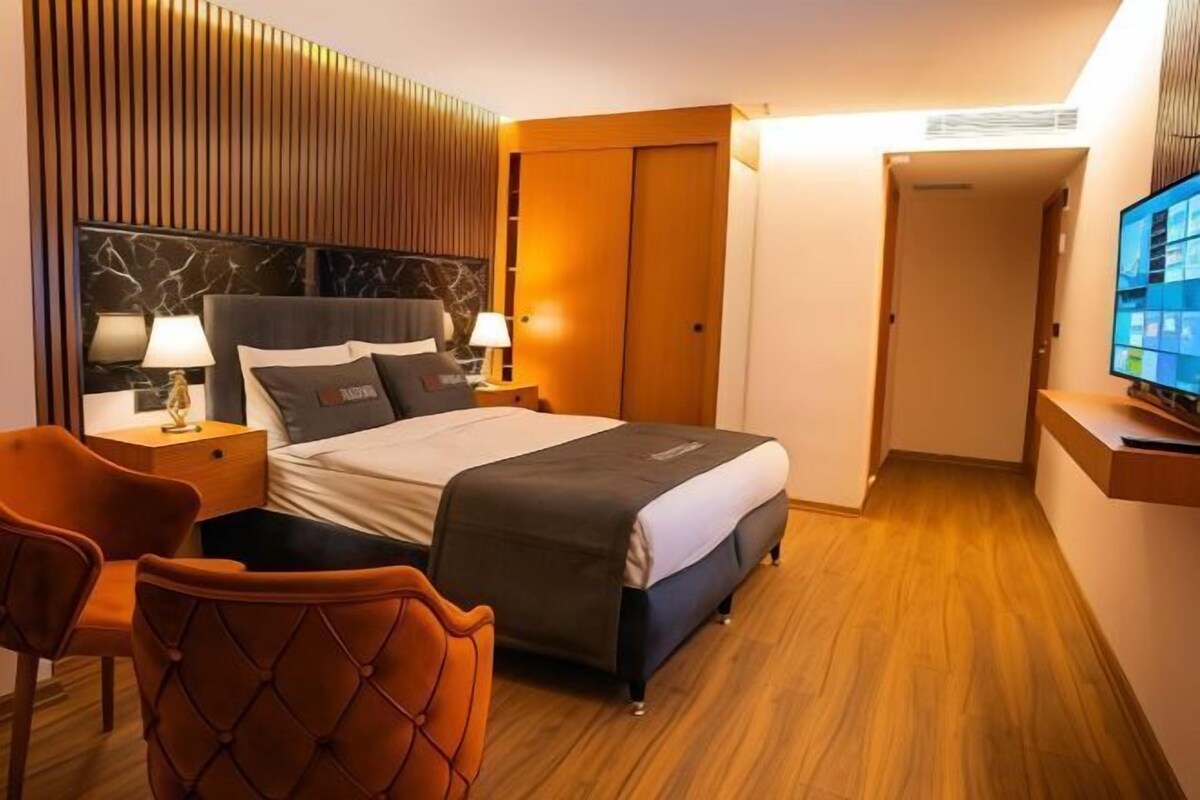 A hotel room with a bed, two bedside tables, a TV, a chair, and a wardrobe.