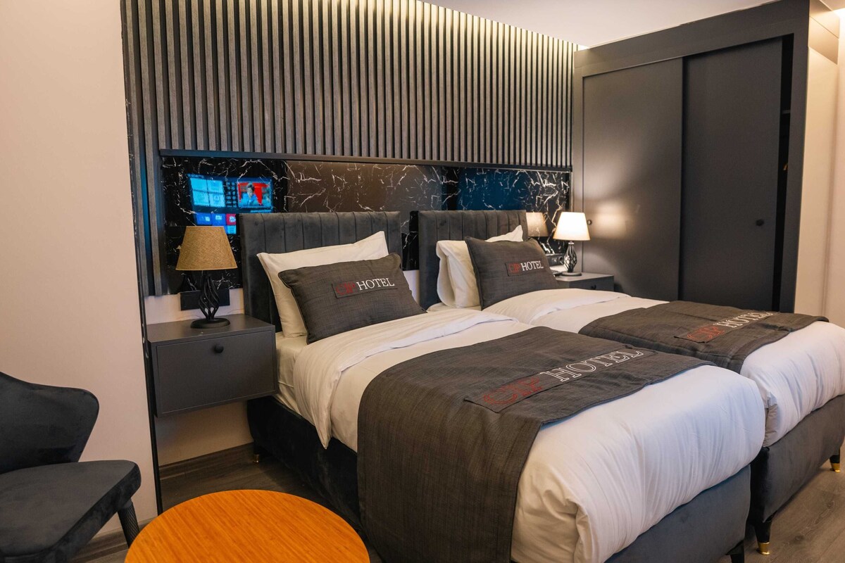A modern hotel room with a large bed, two bedside tables, a TV, and a wardrobe.
