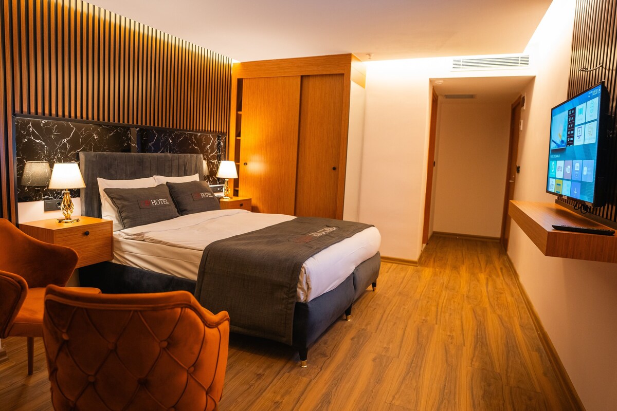 A hotel room with a bed, a desk, a chair, a TV, and a wooden floor.