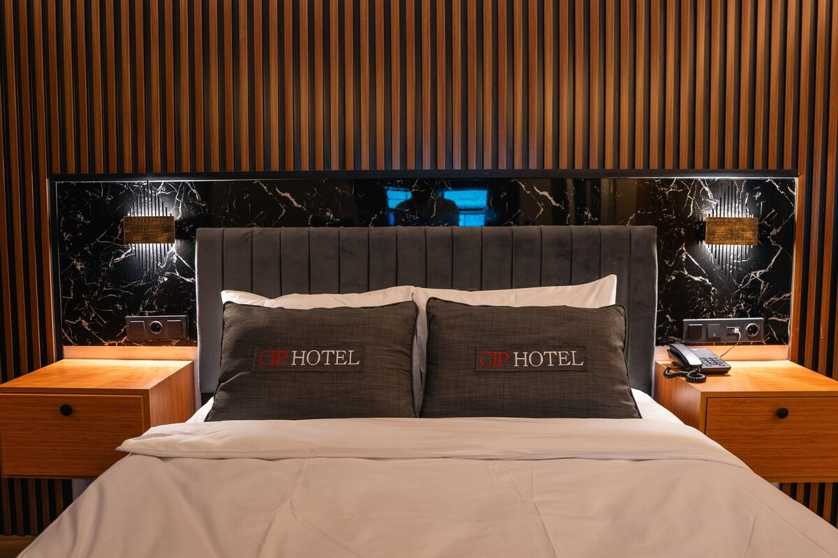 A hotel room with a bed, two nightstands, a wooden headboard, and a marble wall.