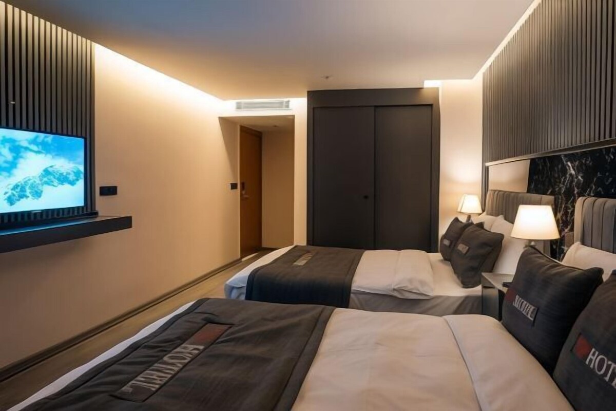 A hotel room with two beds, a TV, a desk with a lamp, and a wardrobe.