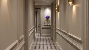 A hallway with patterned flooring, wall-mounted sconces, and a vase with flowers on a pedestal. - Cip hotel istanbul  (Istanbul)