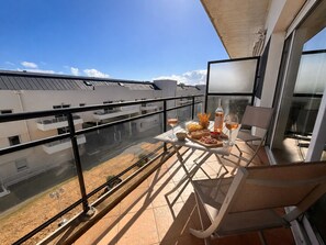A balcony with a table set for a meal, a bottle of wine, and a chair.