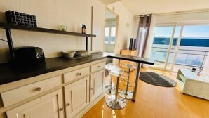 A modern kitchen with a black countertop, white cabinets, and a bar area with stools. - Charming love nest with balcony (La Rochelle)