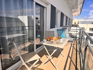 A balcony with a table set for breakfast, including fruits, bread, and drinks.