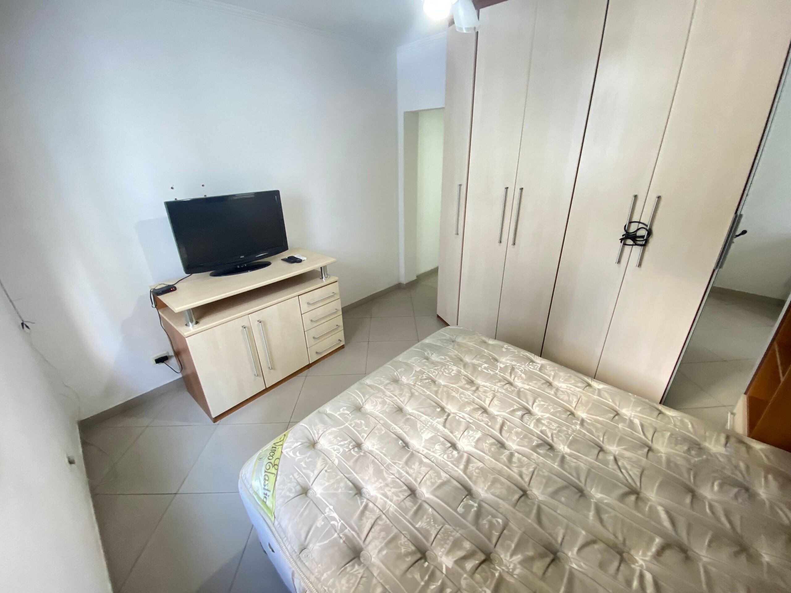 A bedroom with a bed, a TV on a wooden cabinet, and a wardrobe.