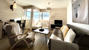 A cozy living room with a sofa, armchair, and a coffee table. There is a TV on a stand and a painting on the wall. - Le Balcon des Princesses (Demi-Quartier)