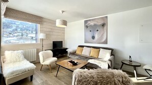A modern living room with a large window, a sofa, a coffee table, and a bear-themed artwork on the wall. - Le Balcon des Princesses (Demi-Quartier)